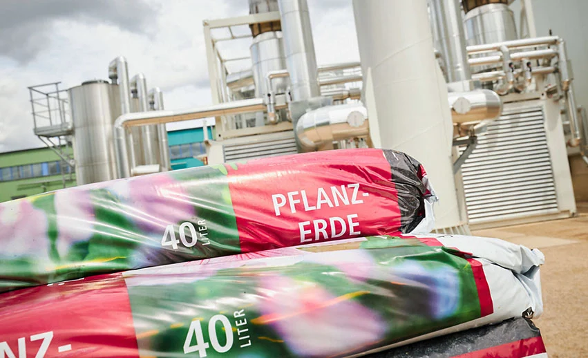 Im Vordergrund 40-Liter-Säcke mit "Pflanzerde" mit einer technischen Anlage im Hintergrund