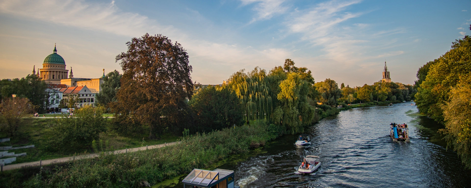 Blick über die Havel auf das baumbewachsende Ufer in Potsdam mit St. Nikolaikirche und sommerlichem Himmel im Hintergrund