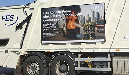 Ein Abfallsammler (Hecklader) der FES mit seitlich angebrachtem Kampagnenmotiv mit einem Foto eines brennenden "Müllfahrzeugs"